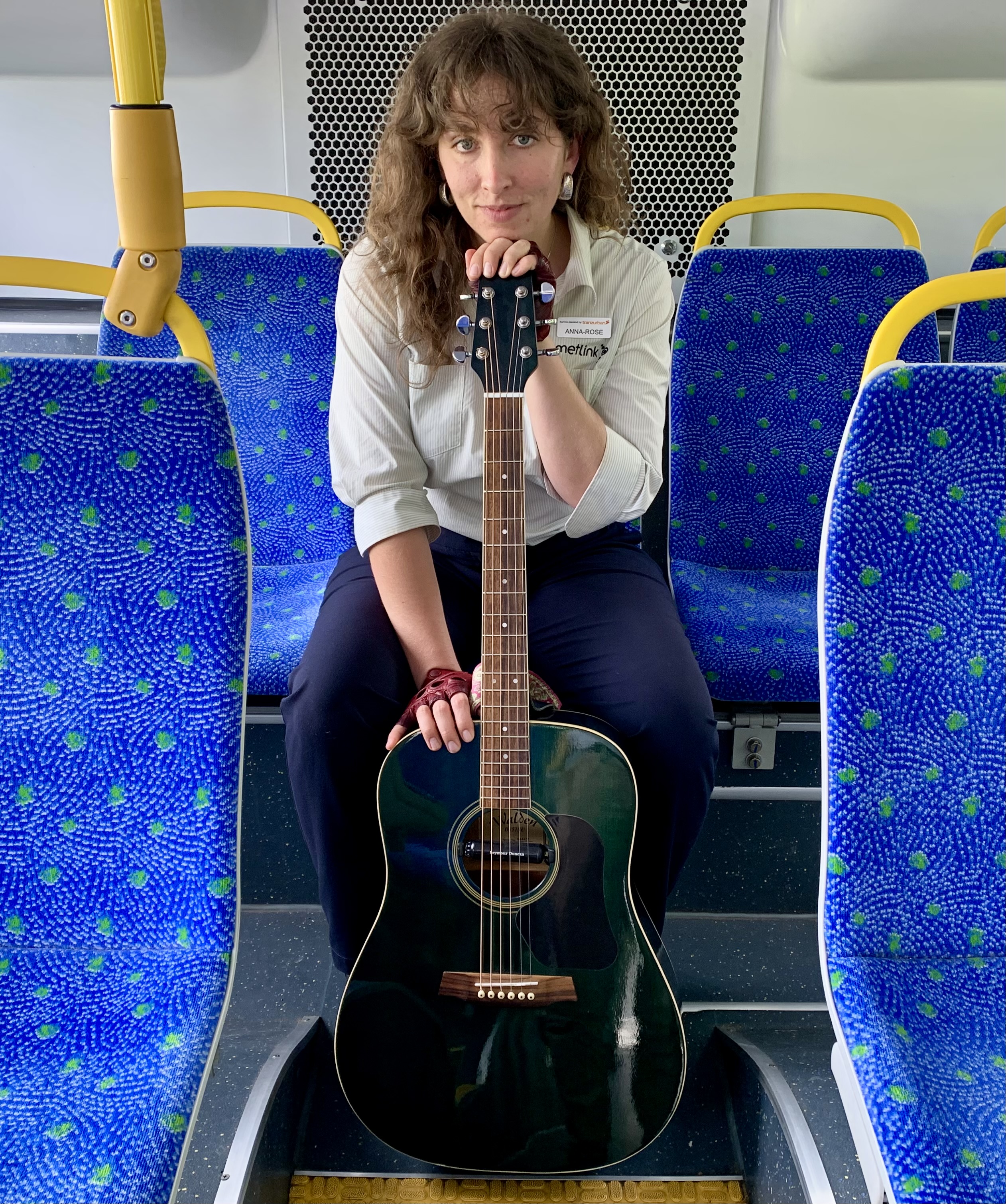 Anna-Rose in the back seat of a bus with her guitar